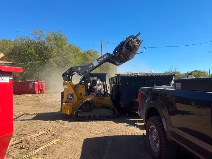 Skid steer dumping debris into a trailer on a land cleanup job